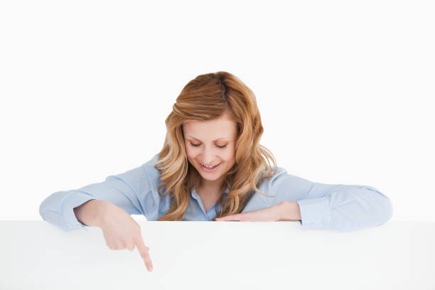 istock Attractive woman pointing at an empty white board below her 826463462