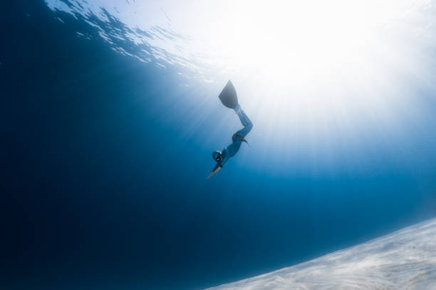 Woman freediver glides over sandy bottom in a tropical clear sea with sun rays