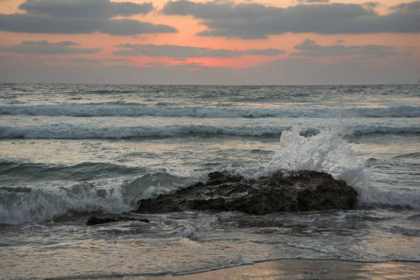 waves crashing against a boulder during sunset - sailboat sunset tel aviv sea imagens e fotografias de stock