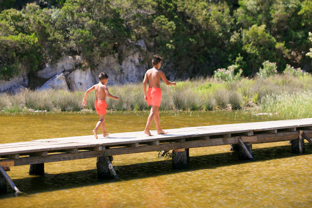 garçon marche sur une passerelle en bois sur un lac - plank boardwalk pontoon bridge summer photos et images de collection