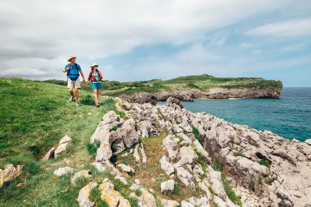 Photo of Couple backpacker travelers walk on ocean rocky coast