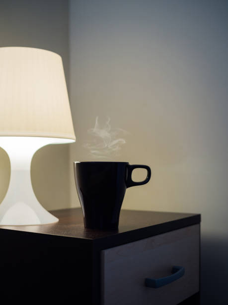 istock Mug with hot steam and lamp on side bed cupboard table, morning and inspiration idea concept background 826571454