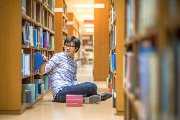 istock Young Asian man university student choosing book in library 826589580