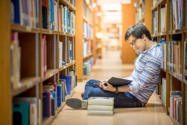 istock Young Asian man university student reading book in library 826589584