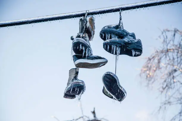 Photo of Frozen Shoes on a line are covered in ice from an ice storm. Many icicles have formed and they are sunlit with this layer of ice.