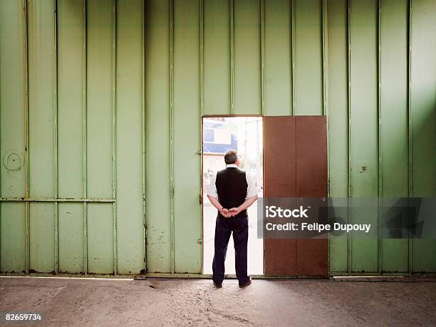 Man Standing In The Door Of A Factory Stock Photo - Download Image Now - Security Guard, Rear View, Hands Behind Back