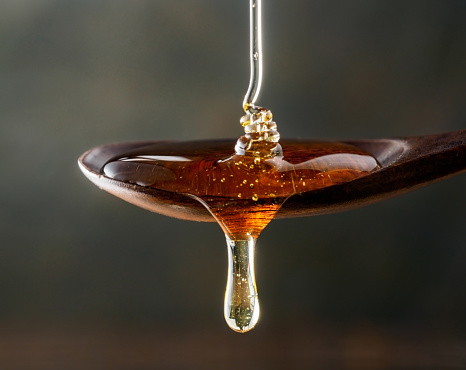 Honey pouring on wooden spoon and dripping from spoon. Dark background. Extreme close up.