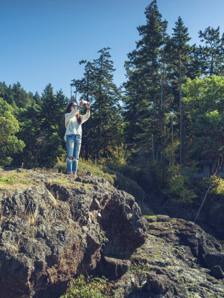 istock woman with camera standing on rocks against blue sea 826613184