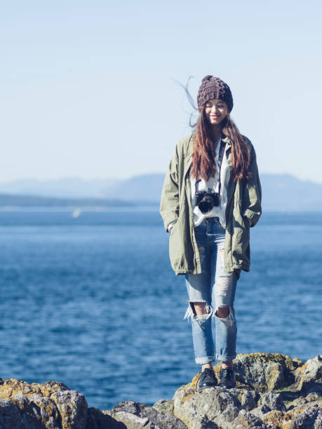 woman with camera standing on rocks against blue sea,usa.