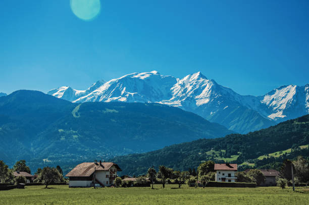 Fields with houses, forest, alpine landscape and blue sky in the background, Saint-Gervais-Les-Bains, French Alps