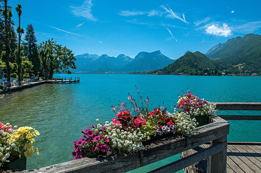 Pier with flowers on the lake of Annecy, in the village of Talloires. Mountains landscape and blue sky on background. France