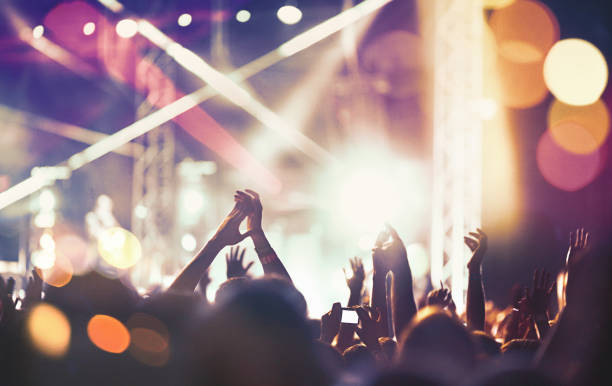 Cheering crowd at a concert. Closeup rear view of large group of people enjoying an open air concert on a summer night. There are a lot of hands raised. Blurry stage lights in background.  disco dancing photos stock pictures, royalty-free photos & images