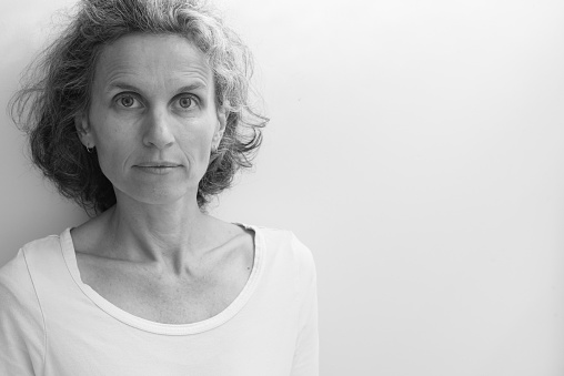 Portrait of natural looking middle aged woman against neutral background with copy space to right (black and white, selective focus)