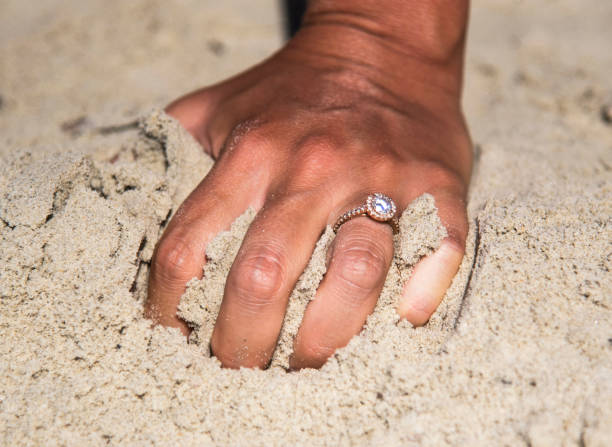 istock Woman's hand with a diamond ring in the sand 826654000