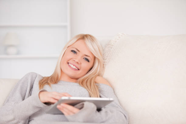 istock Pretty blond woman lying on a sofa relaxing on a line of tablet computers 826680596