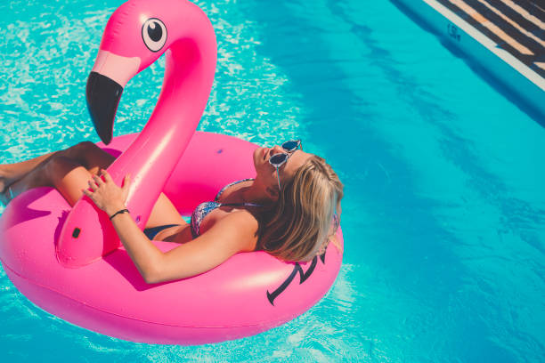 Sexy girl in bikini wearing sunglasses on inflatable flamingo Attractive blonde caucasian woman at the pool, floating on a inflatable pool toy, enjoying time in the summer, vacations in a popular travel destination, taking care of her body inflatable ring photos stock pictures, royalty-free photos & images