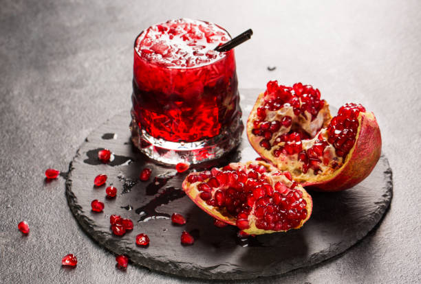 istock A refreshing fruity beverage and a cut garnet on a gray background. Red non-alcoholic drink with ice. Fresh bittersweet beverages. 826719778