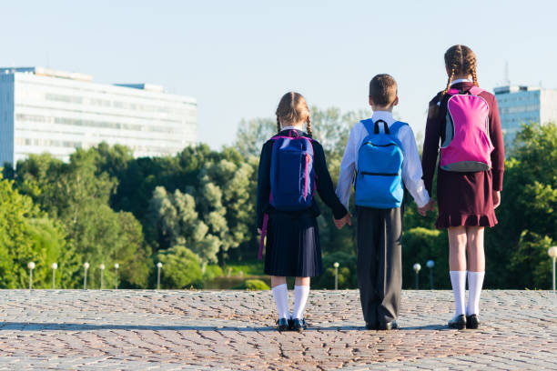 istock Three pupils in school uniform stand on the street with backpacks, rear view 826720200