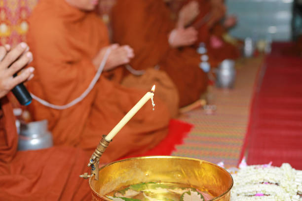 Monk makes holy water with candle in golden bowl.
