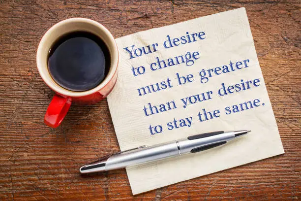 Your desire to change must be greater than your desire to stay the same - inspirational handwriting on a a napkin with a cup of coffee