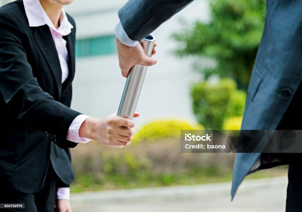 Business people passing baton Businesswoman passing baton to a businesswoman outdoors. Relay Baton Stock Photo