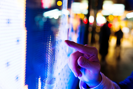 Man finger pointing at LED screen of stock market price at night.