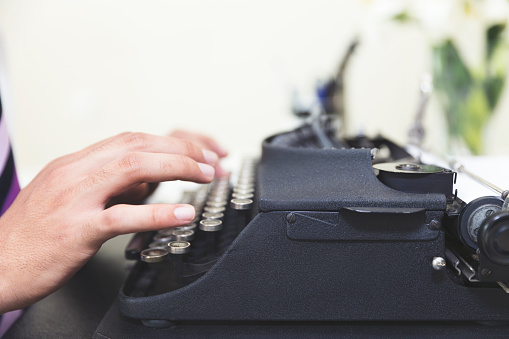 Unrecognizable author hard at work in completing his novel on his typewriter from a home office.