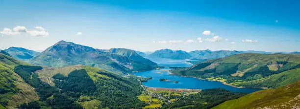 Panoramic vista across the green summer mountains of the Highlands from the tranquility of Glencoe village to the blue shores of Loch Leven and Loch Linnhe, Lochaber, Scotland.