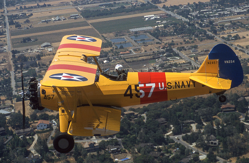 Air to air shot of Boeing-Stearman Model 75 flying over mixed farmland and residental properties.\n\n