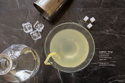 Flat lay Lemon Drop martini in stemmed glass with sugar cubes, shaker and bottle garnished with a twist.