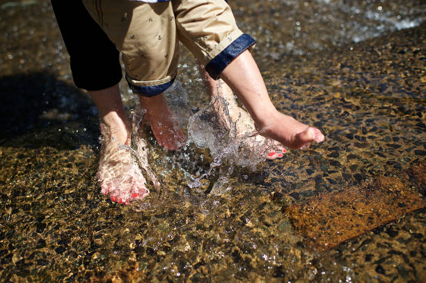Feet of a young boy kicking water and a woman with red toe nails in a clear flowing water mountain stream Stellenbosch Cape Town South Africa