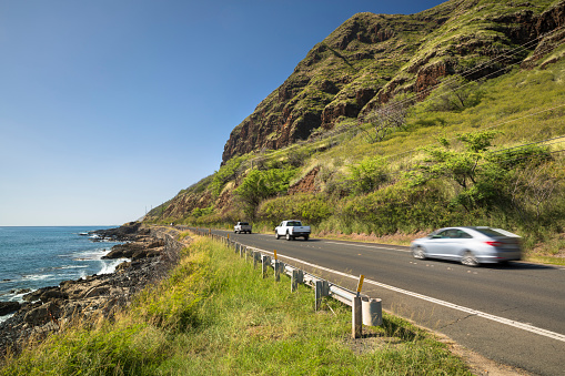 Cars drive down the Farrington highway  by Kaena Point State Park and Keawaula beach in Oahu Hawaii USA
