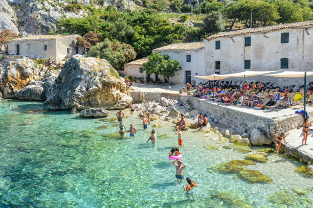 Scopello beach in Sicily, Italy Beachgoers enjoy their summer vacation in the Italian resort town of Scopello. Photo taken during a hot summer day and features people walking, swimming, and suntanning by the water. cefalu stock pictures, royalty-free photos & images