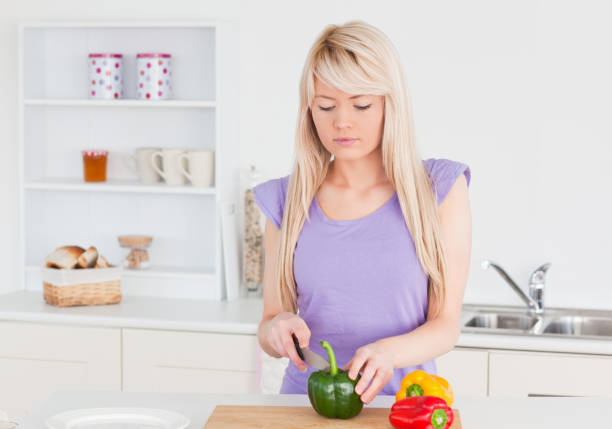 istock Smiling blonde woman cutting vegetables in modern kitchen interior 826883054