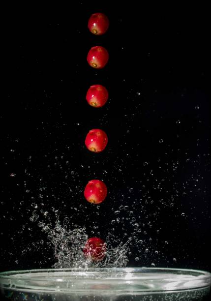 rote kugel traube auf wasser fallen - stroboscopic image stock-fotos und bilder