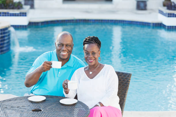 pareja senior afroamericana por piscina tomando café - upper class wealth women senior adult fotografías e imágenes de stock