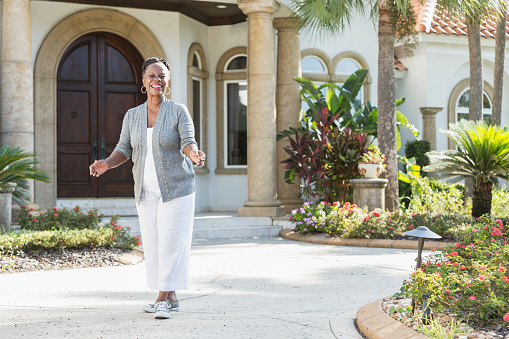 A happy senior African-American woman in her 60s standing outdoors, in front of her home, smiling confidently at the camera.