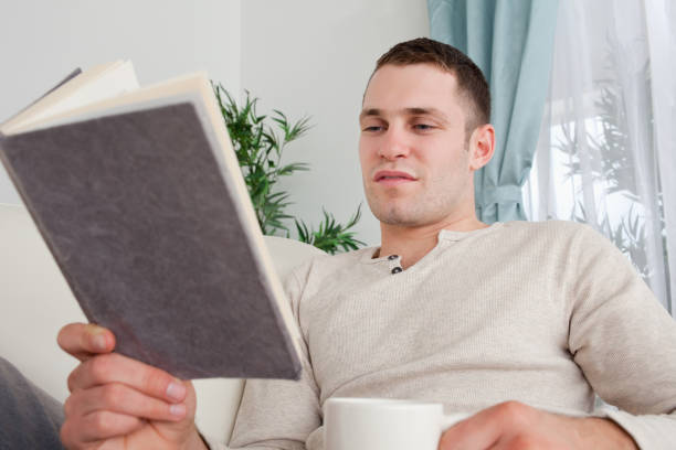 istock Man reading a book while holding a cup of tea 826938924