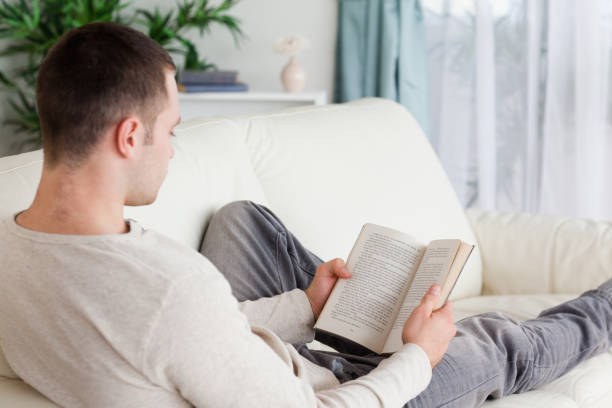 istock Portrait of a man lying on his couch reading a book 826939112