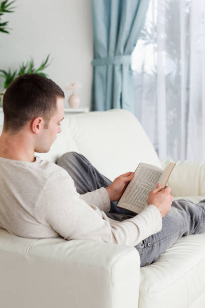 istock Portrait of a man lying on a sofa reading a book 826939170