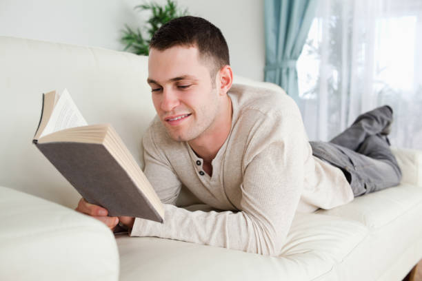 istock Young man lying on a couch to read a book 826958656