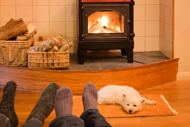 Socks and feet of a couple relaxing by fire in woodburner with west highland terrier - focus is on dog and stove