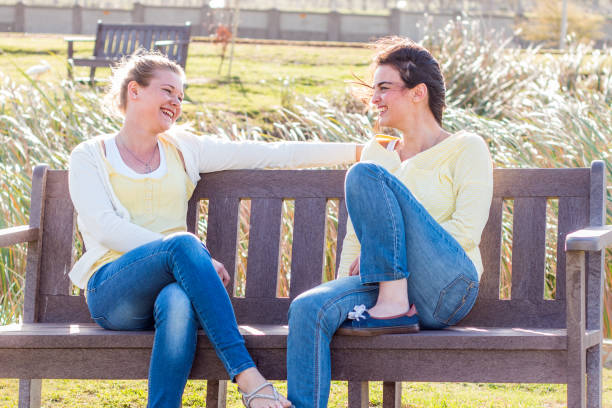 istock Two friends sitting on bench in park talking, laughing and having fun. 826978620