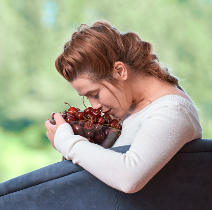 profile view of young woman smelling bowl of fresh cherries.
