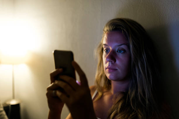 istock Woman with thoughtful expression sitting on bed, using mobile phone 827002988
