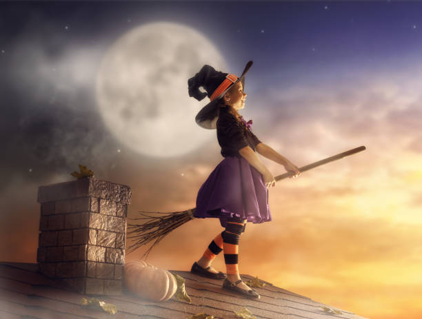 Happy Halloween! Cute little witch with a broomstick. Beautiful young child girl in witch costume on the roof.