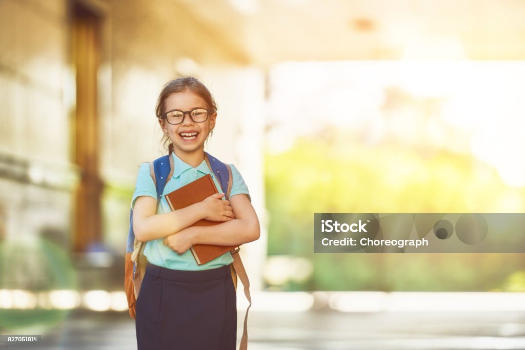 Girl with backpack Pupil of primary school with book in hand. Girl with backpack near building outdoors. Beginning of lessons. First day of fall. Child Stock Photo