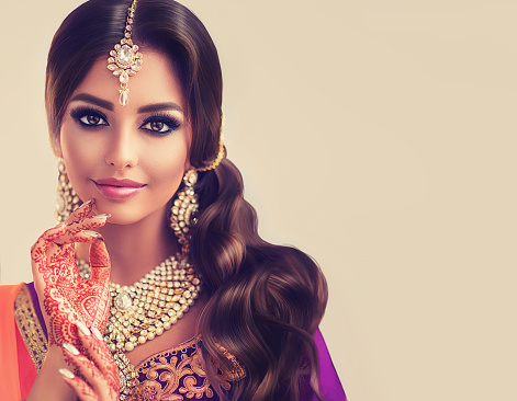 Portrait of beautiful indian girl dressed in a traditional national suit,  mehndi henna tattoo is  painted on her hands and traditional kundan style jewelry set. Black haired indian young woman put on  in a posh outfit lehenga choli.