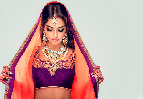 Portrait of beautiful indian girl dressed in a traditional national suit-sari,  mehndi henna tattoo is  painted on her hands and traditional kundan style jewelry set. Black haired indian young woman put on  in a posh outfit lehenga choli.