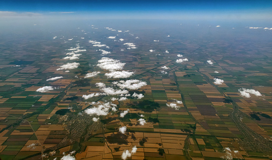 A wide angle aerial view of curly sunny clouds and their shadows on mosaic landscape.